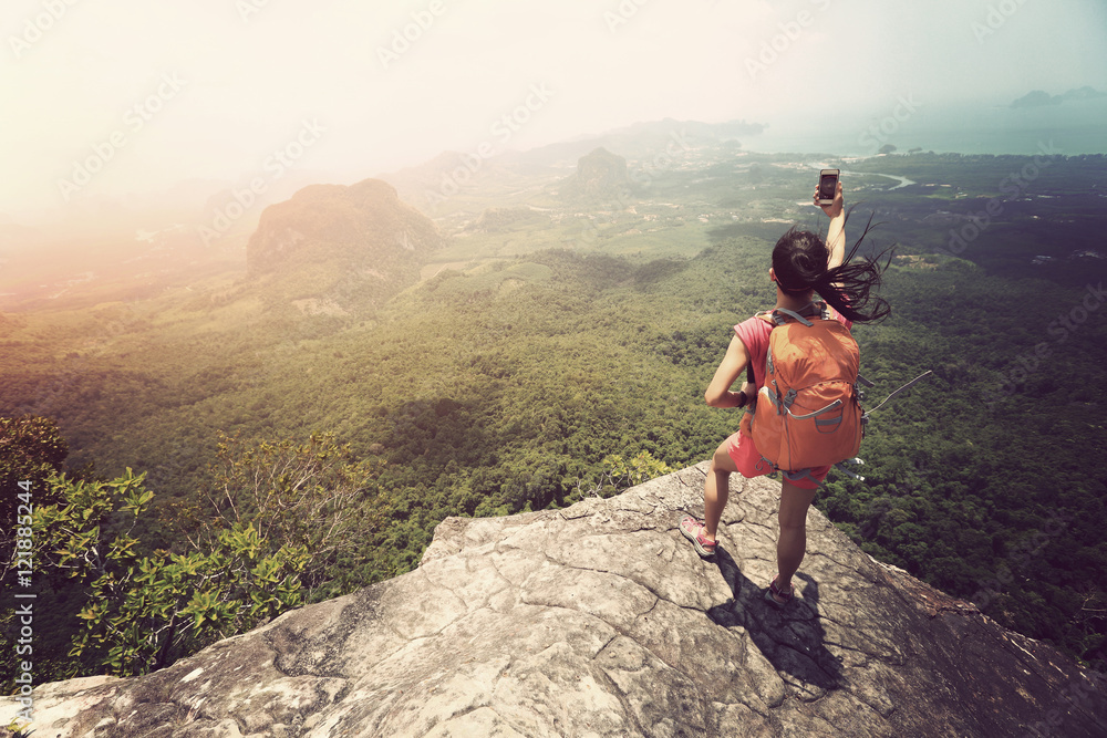 Obraz premium young woman hiker taking photo with smartphone on mountain peak cliff