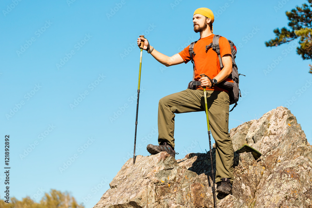 Young male with beard is traveling through the mountain, tourist rucksack standing on rock hill while enjoying nature view, summer holidays in mountains