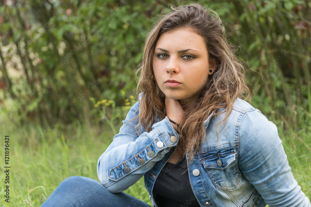 Portrait of a pensive young woman sitting outside. Girl is looking at the camera. Portrait of a pensive young woman sitting outside. Girl is looking at the camera.