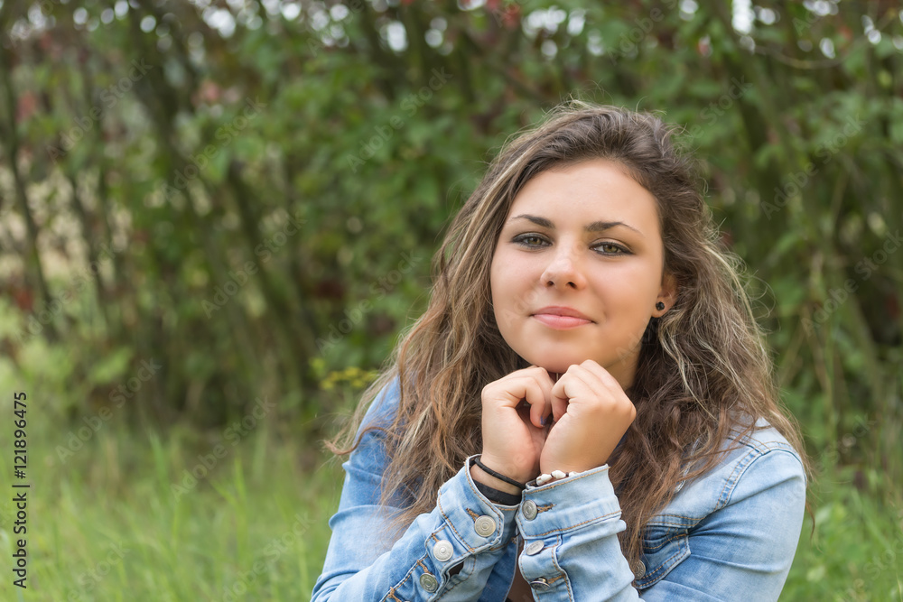 Portrait of brunette teenage girl sitting outdoors. Girl is supporting her chin by fists