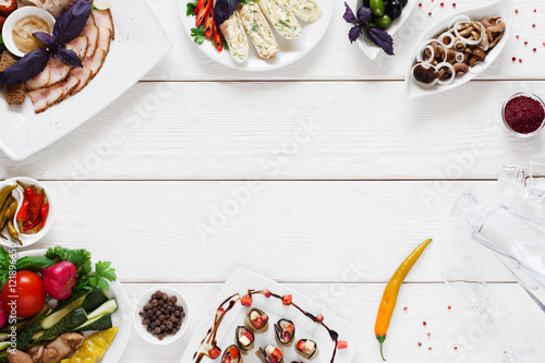 Variety of snacks for traditional tableful, free space. Delicious homemade meals with glass decanter with vodka on white wooden background, flat lay, copy space, frame