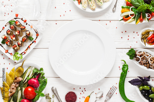 White ceramic plate surrounded by snacks, void. Variety of vegetarian meals make frame for empty dish. Cuisine, menu, food concept