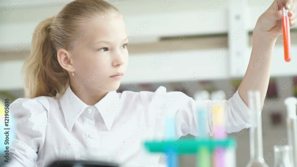 Serious teen girl doing homework. 11-13 years old girl. Girl sitting at a desk and writing something. Schoolgirl. Pupil. Stand on the desk with test tubes. Girl doing chemistry experiment Serious teen girl doing homework. 11-13 years old girl. Girl sitting at a desk and writing something. Schoolgirl. Pupil. Stand on the desk with test tubes. Girl doing chemistry experiment