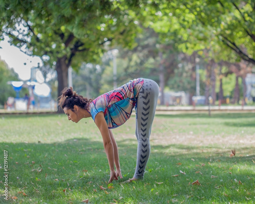 Young woman practicing yoga in the park on the green grass with