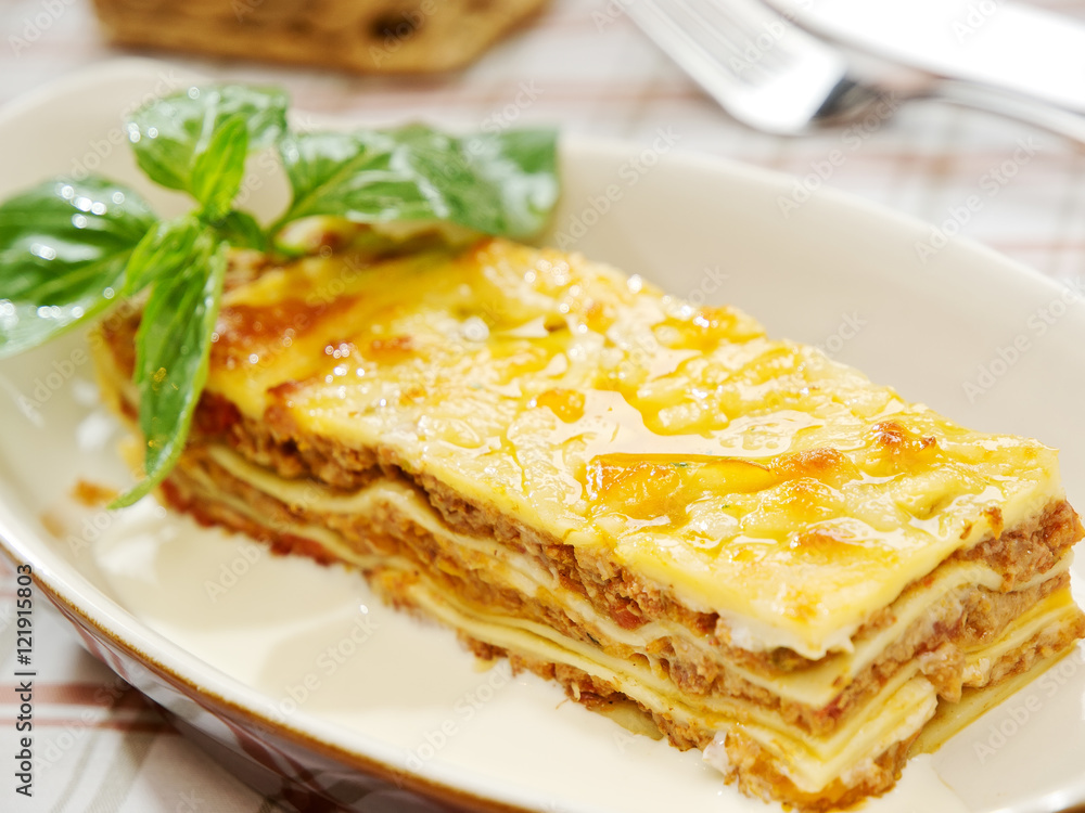 Traditional lasagna made with minced beef bolognese sauce topped with basil leafs served on a white plate