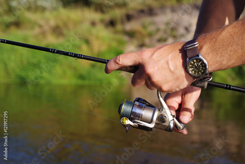 Fishing with a spinning on the river. Man catches fish, a close up of a hand and the spinning reel.