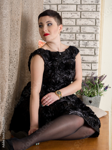 girl in a black dress with short hair at the window on the brick wall background