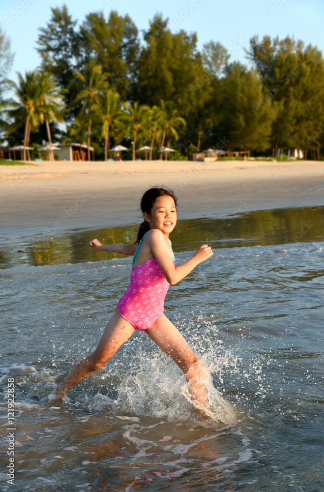 Happy young Asian girl running and jumping in the waves during summer vacation on exotic tropical beach. Kids play at the sea. 