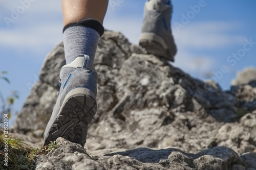 Close up of hiking boots and legs climbing up rocky trail and reaching the top of a mountain