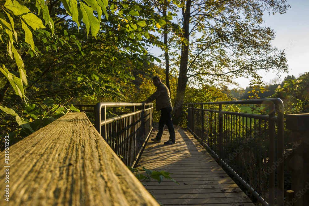 Mann hält beim Spazierengehen auf einer Brücke inne Mann hält beim Spazierengehen auf einer Brücke inne