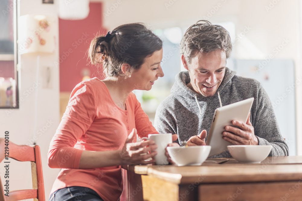 Nice couple using a tablet while having breakfast in the kitchen Nice couple using a tablet while having breakfast in the kitchen