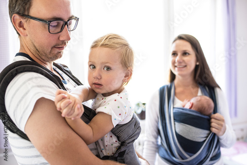 Young parents with children in sling and baby carrier