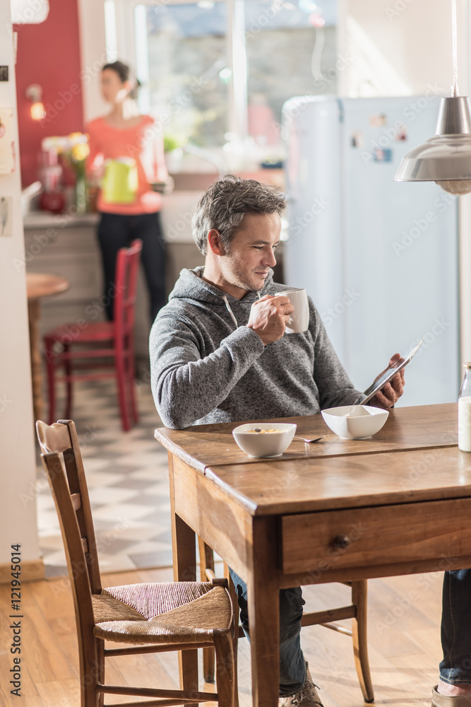 Nice couple using a tablet while having breakfast in the kitchen Nice couple using a tablet while having breakfast in the kitchen