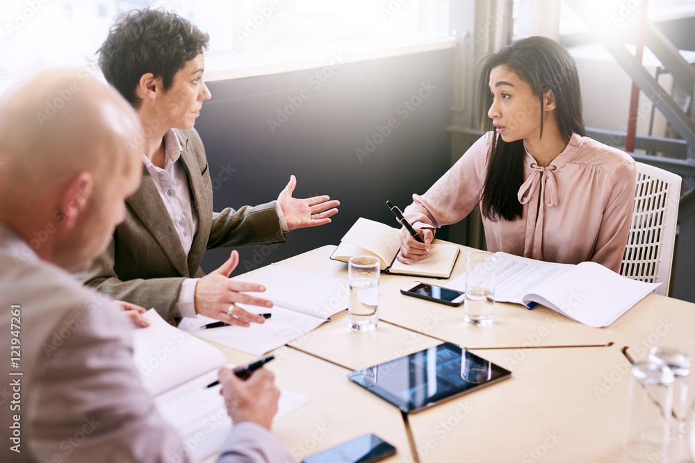 Business meeting between three executive employees, two female and one male, taking place in a birght conference table early in the morning to prepare for the week ahead. Business meeting between three executive employees, two female and one male, taking place in a birght conference table early in the morning to prepare for the week ahead.