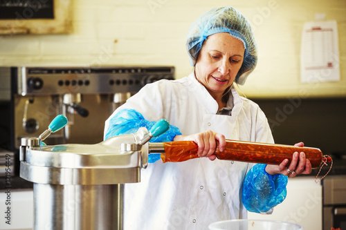 Woman working in a butchery, wearing protective clothes and gloves, filling a casing with Chorizo sausage meat. photo