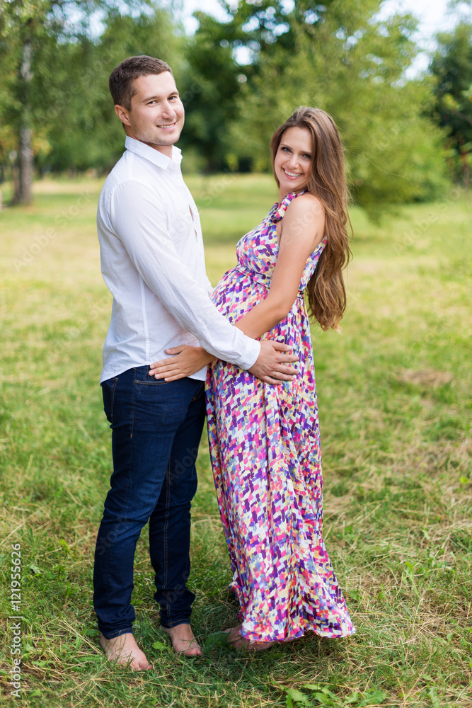Beautiful pregnant couple happy together expecting a child. Man and woman walking in the park. Share the love and family, love concept.