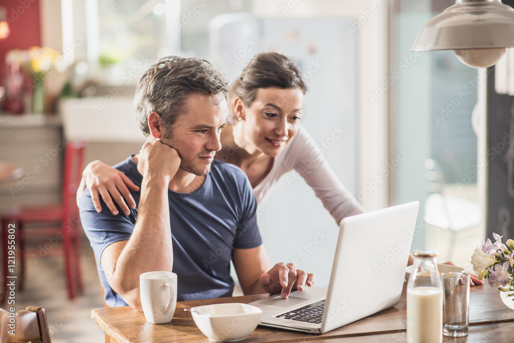 A couple using a laptop while having breakfast in the kitchen A couple using a laptop while having breakfast in the kitchen