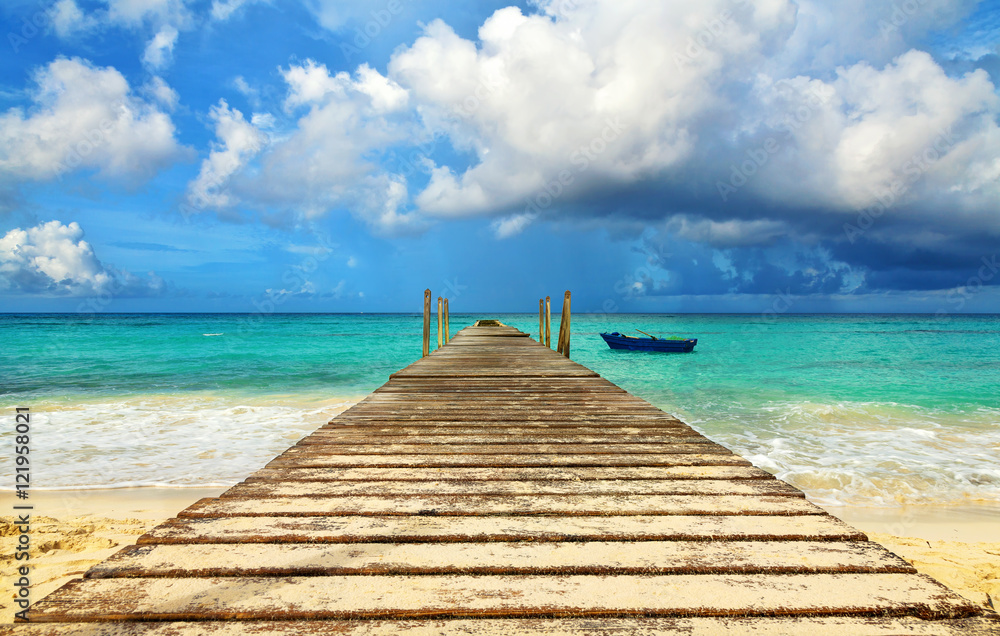 Perspective view of a wooden pier on the seashore with clear blue sea. Fishing boat at the sea coast of the Dominican Republic. Blue fishing boat.
