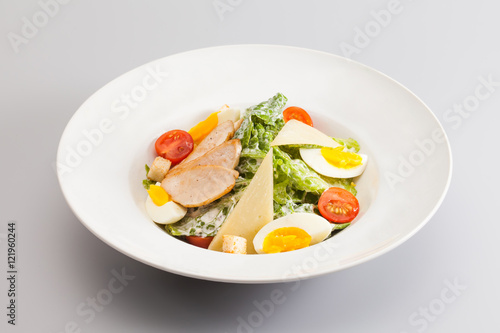 Caesar salad with chicken breast tomato cherry, eggs. white plate gray background. horizontal photo