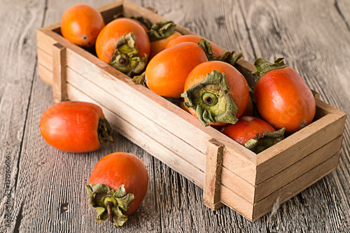   Persimmon.   Juicy ripe persimmon in a wooden box on a gray wooden background. photo