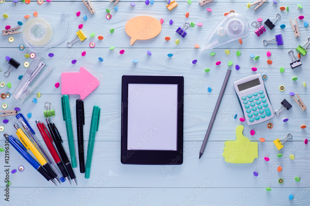 Office, business, education still life concept on blue wooden background. Top view of wooden desktop with e-book and bright colorful stationery items. Set of mock up e-book and stationery, flat lay. Office, business, education still life concept on blue wooden background. Top view of wooden desktop with e-book and bright colorful stationery items. Set of mock up e-book and stationery, flat lay.