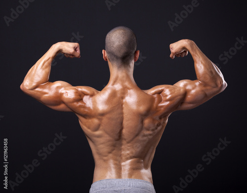 Back view of a male bodybuilder flexing his biceps on black back