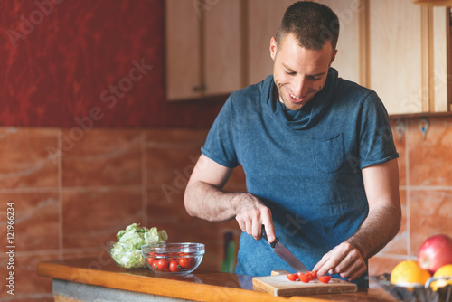 Happy man in kitchen making vegetable salad.