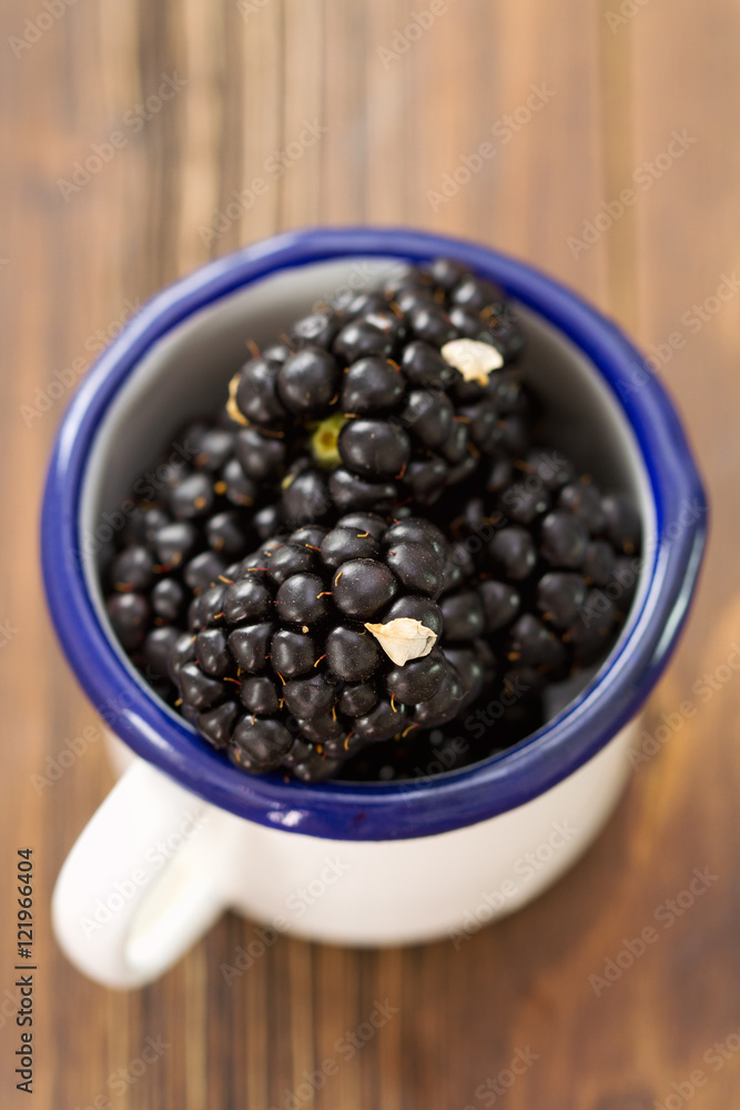 blackberries in white cup on brown wooden background blackberries in white cup on brown wooden background