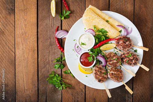 Appetizing kofta kebab (meatballs) with sauce and tortillas tacos on a white plate. Top view photo