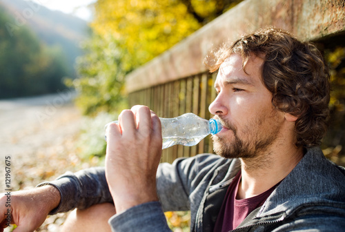 Young handsome runner with water bottle sitting on a bridge