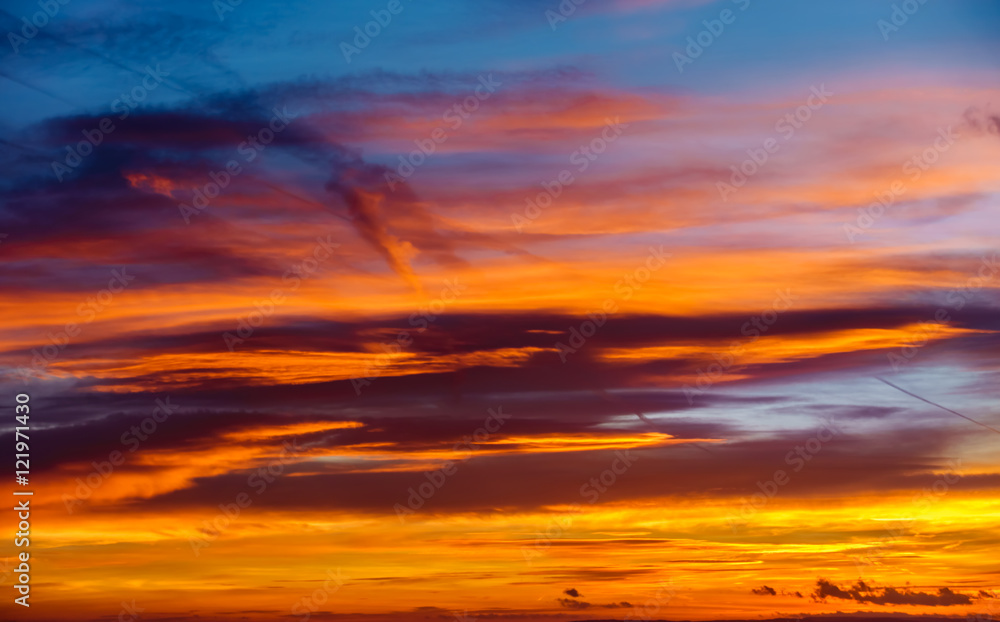 
Dramatic sunrise sky in a mixture of dark blue, orange, red, yellow and golden colours with dark clouds.