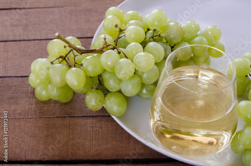 bunch green grapes with glass of white wine on white plate, food closeup