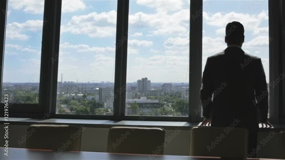Young businessman looking through a large window at the city and cloudy sky. Young businessman looking through a large window at the city and cloudy sky.