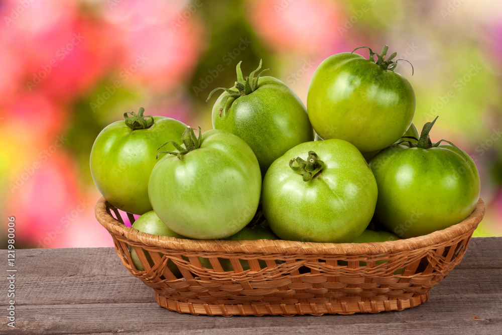 unripe green tomatoes in a wicker basket on wooden table with blurred background unripe green tomatoes in a wicker basket on wooden table with blurred background