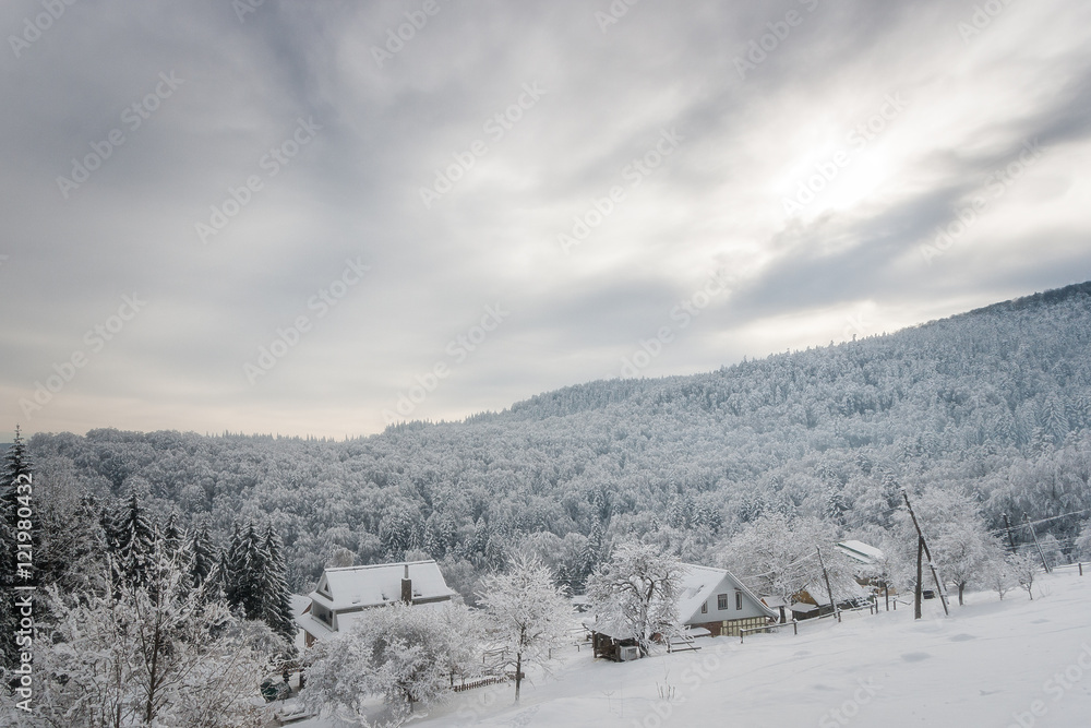 Beautiful winter landscape with a house on  background of snow-covered forests and mountains.