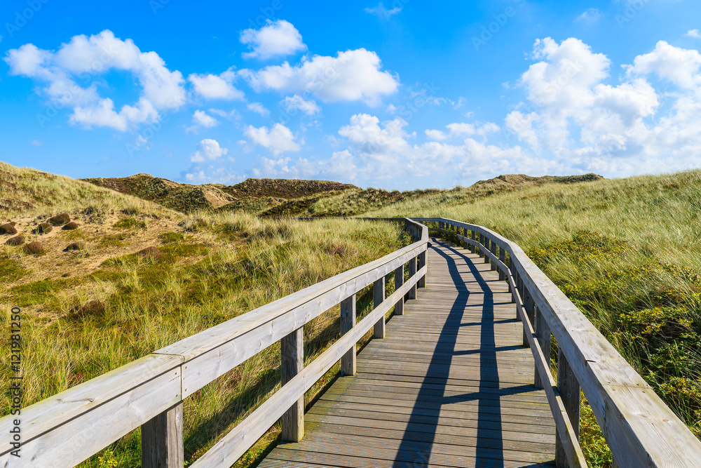 Wooden walkway to beach among sand dunes and sunny blue sky with white clouds, Sylt island, Germany