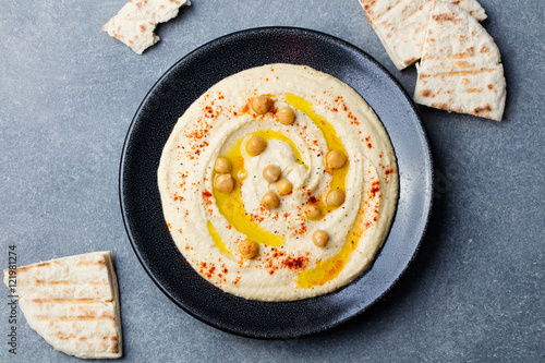 Fotografie Hummus, chickpea dip, with spices and pita, flat bread in a black plate