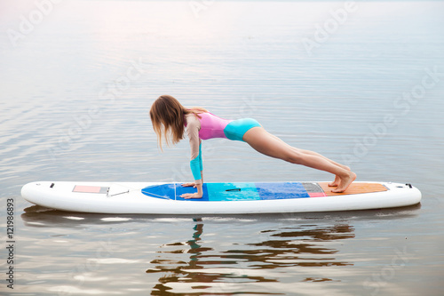 Woman doing yoga on sup board with paddle