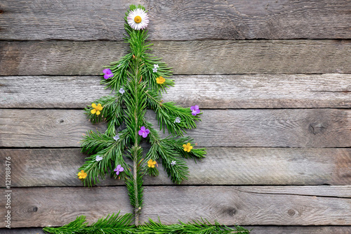 Hand made fir tree from evergreen branches. Decoration yellow and pink wildflowers. Creative idea for christmas scene.