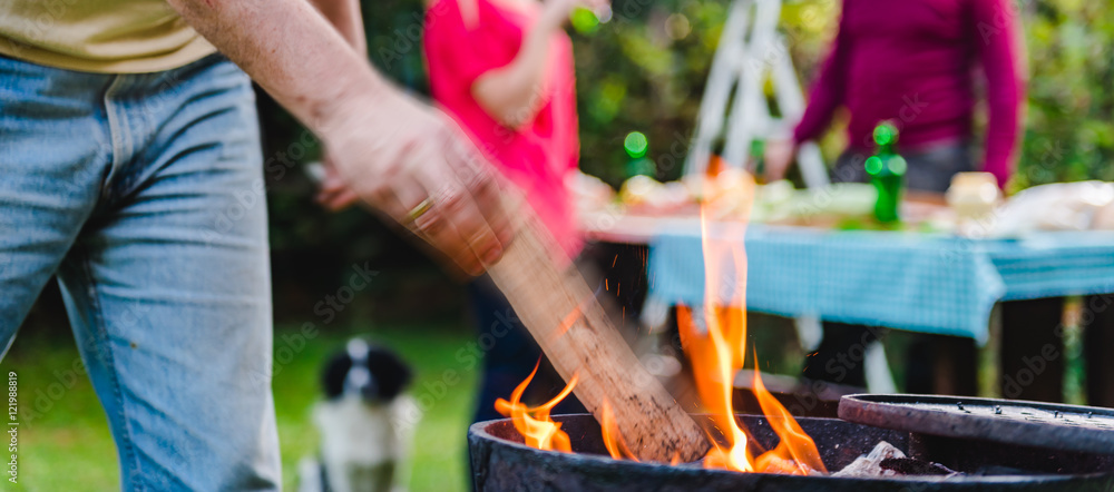 Man on a lawn putting firewood into barbecue