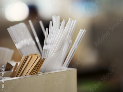 Plastic transparent straws, wooden sticks for coffee and drinks, and sugar over blurred background