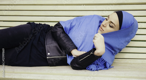 muslim girl. young woman in a blue scarf lying on park bench