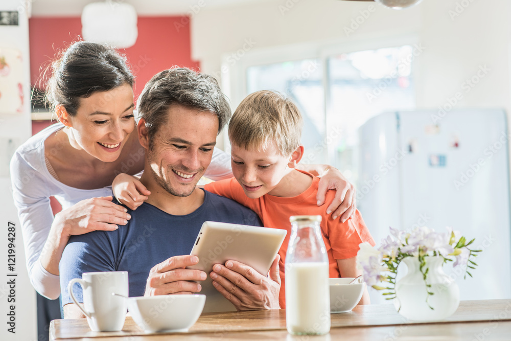 A family using a tablet while having breakfast in the kitchen A family using a tablet while having breakfast in the kitchen