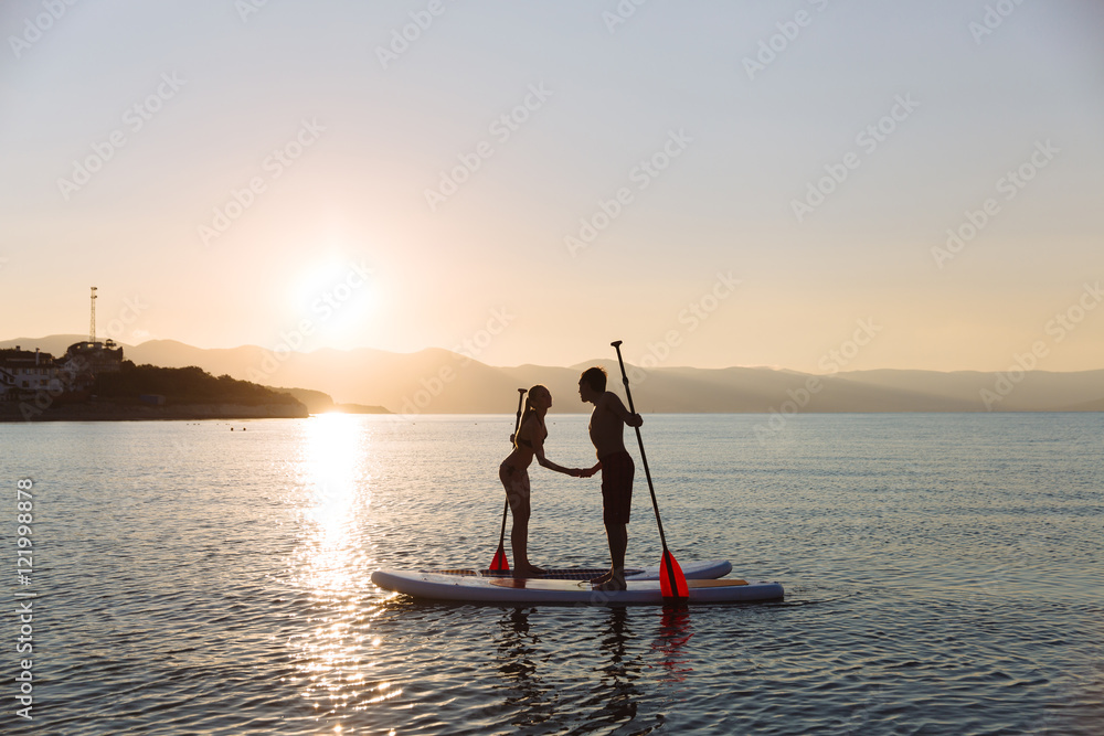 Silhouette of kissing male and female on sup surf at the ocean. Concept lifestyle, sport, love
