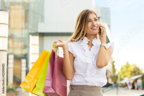 Beautiful young businesswoman in white blouse talking on a mobile phone after doing shopping