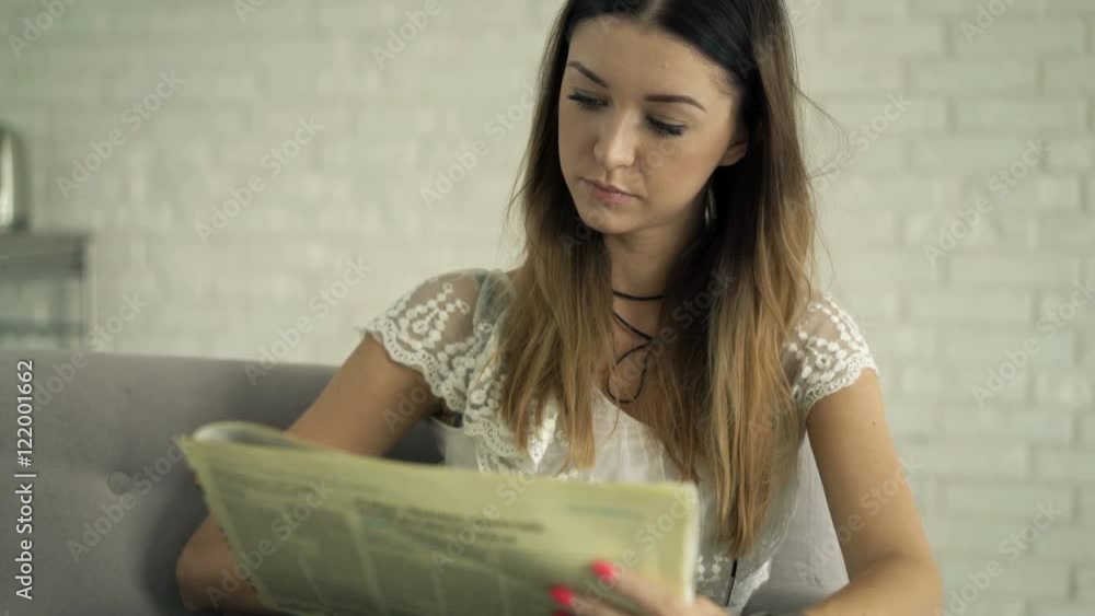 Young woman reading newspaper sitting on sofa at home
Young woman reading newspaper sitting on sofa at home