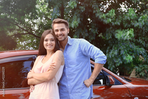 Beautiful young couple standing near red car