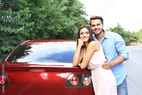 Beautiful young couple standing near red car © Africa Studio