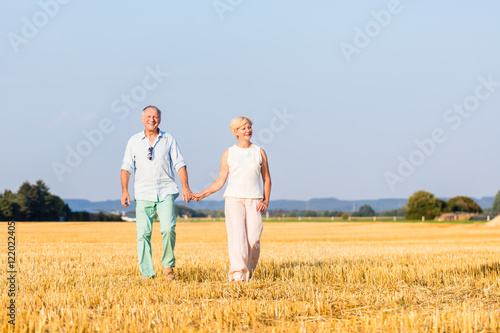 Senior Frau und Mann halten Hände beim Spaziergang über ein Feld © Kzenon