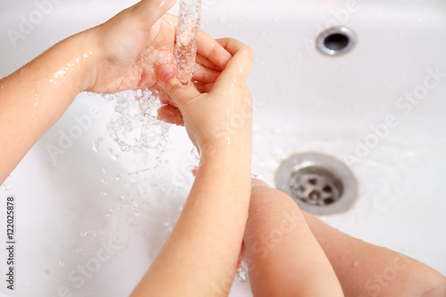 Children washing hands in a white sink under running water
